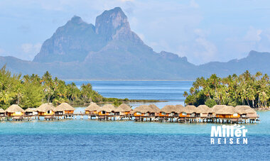 Overwater Bungalows, dahinter eine Insel mit hohen Bergen